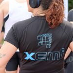 Reprezentantka drużyny XEMI Team podczas biegu charytatywnego Plum Ekiden. Widok pleców w czarnej koszulce z niebieskim logo XEMI i w słuchawkach