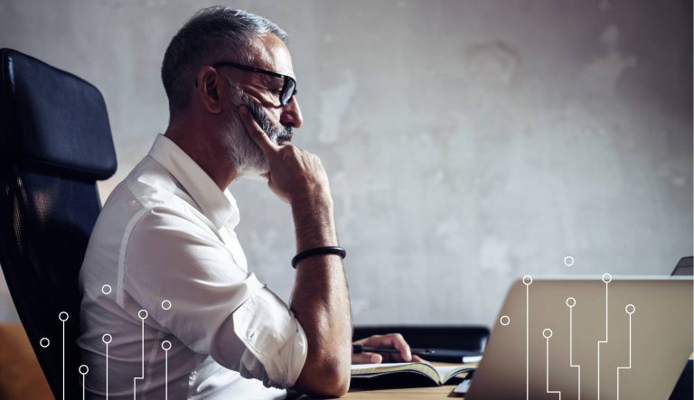 Mężczyzna przy biurku analizuje dane na laptopie, porównując ceny systemów informatycznych.