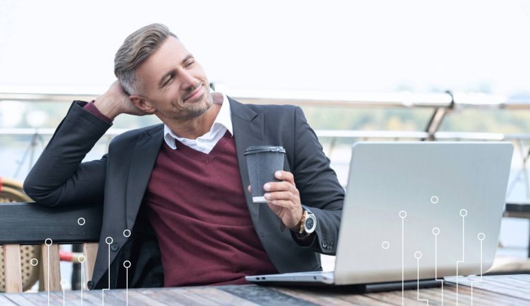 Zadowolony przedsiębiorca po tym jak skutecznie wdrożono u niego system informatyczny. Mężczyzna pracujący zdalnie na laptopie z kawą w ręku.