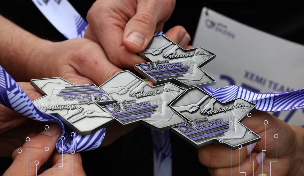 Medale sztafety charytatywnej Plum Ekiden trzymane przez uczestników z zespołu XEMI TEAM i XEMISIE, symbolizujące współpracę, zaangażowanie i wsparcie inicjatyw społecznych.