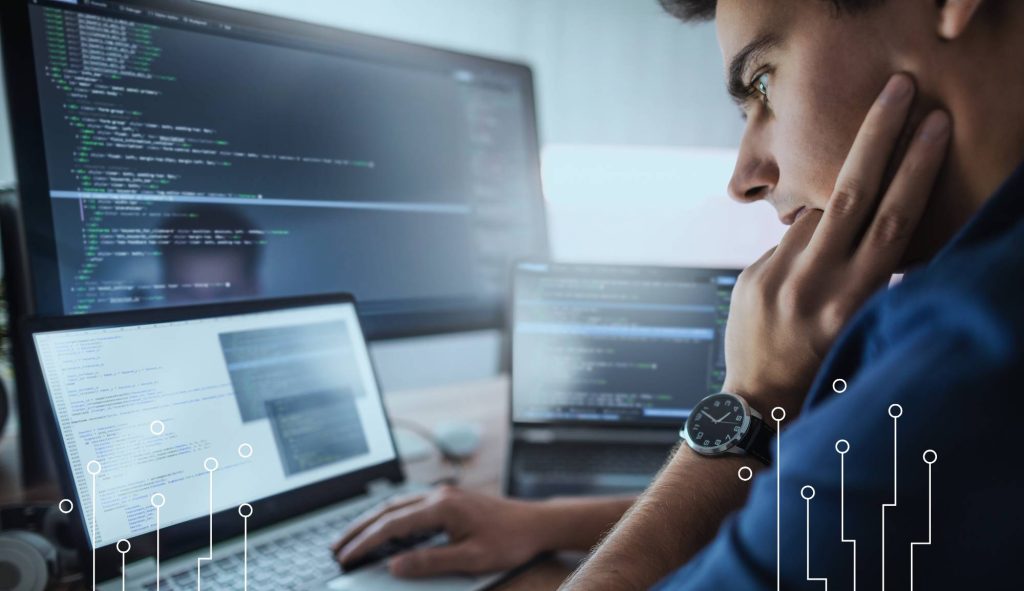 Programista analizujący kod źródłowy systemu IT na monitorze komputera. Opieka autorska oprogramowania, rozwój systemów informatycznych, aktualizacje, utrzymanie oraz wsparcie techniczne po wdrożeniu.